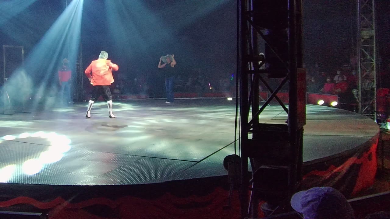 Orange-shirted dancer moves across the stage under angled beams.
