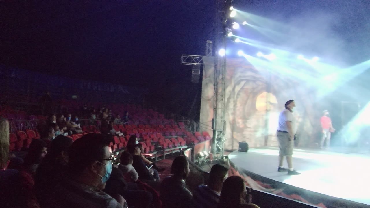 Red seating and audience silhouettes fill the left side as a performer stands on the illuminated stage at right in San Jose del Cabo, Mexico.