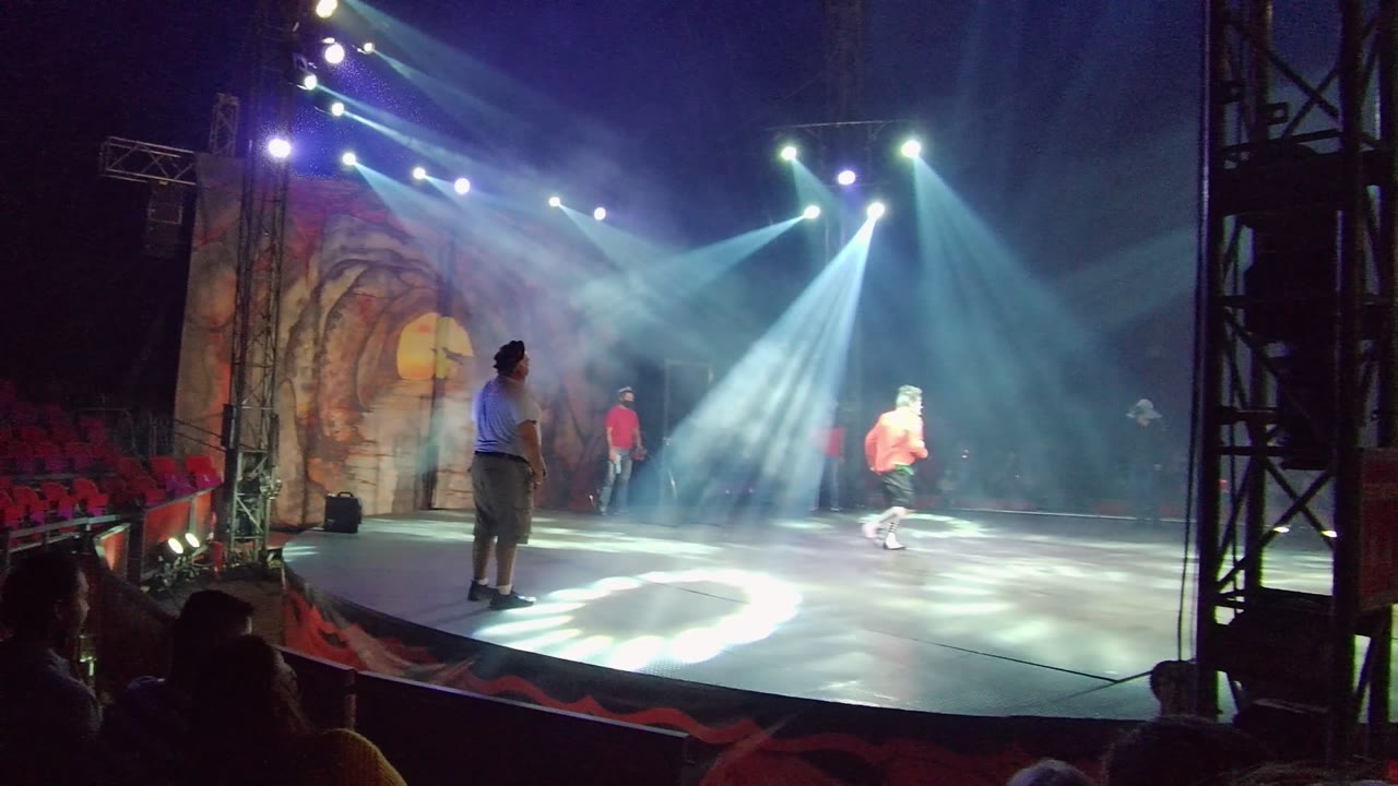 Dancer crosses the lit stage while spotlights cut through haze.