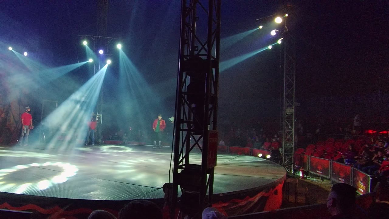 Side view of a San Jose del Cabo stage show with dancers spaced across the stage, white spotlights cutting through fog, and audience seating visible behind them.