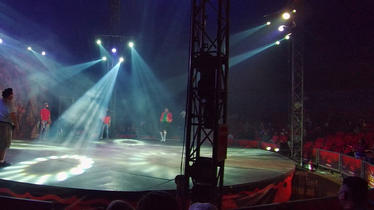 Performer in a blue shirt stands near the side of the lit stage.