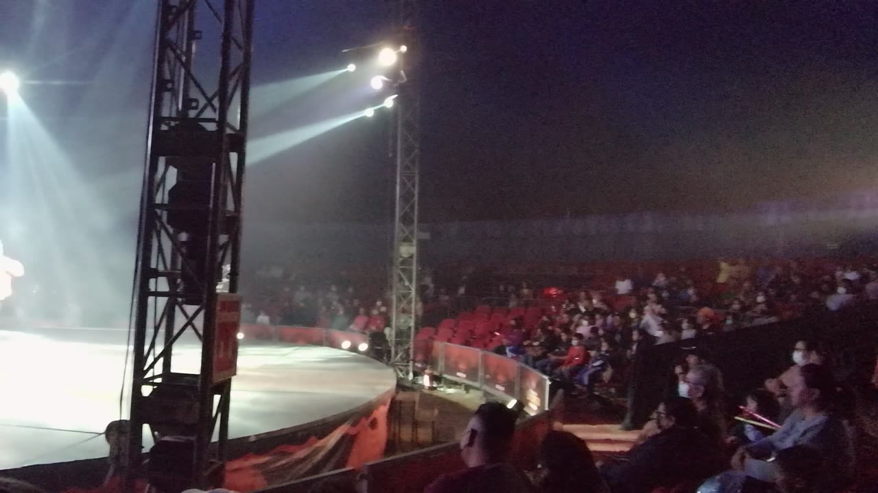 At 0:02 in San Jose del Cabo BCS Mexico, a bright wash of stage light flares across the right side while the audience remains visible in red seating behind the ring.