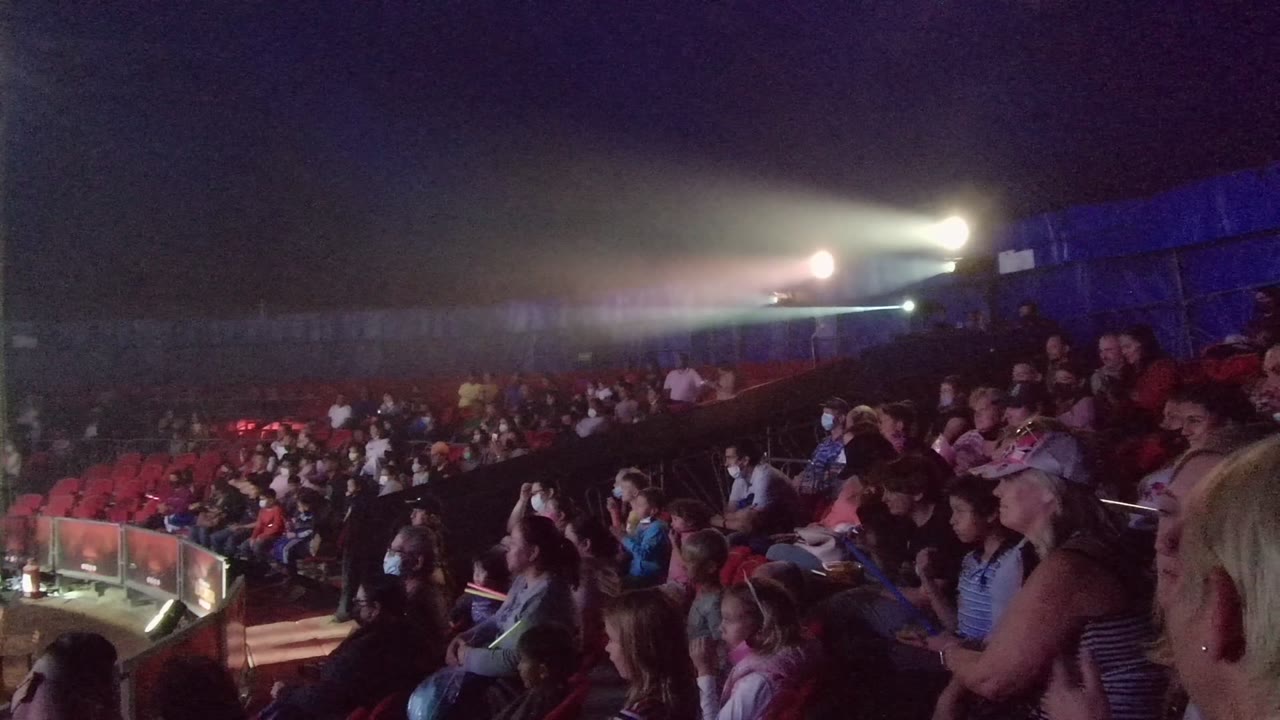 A dim San Jose Del Cabo theater audience sits in red seats while bright stage lights flare across the upper background at the start of the clip.