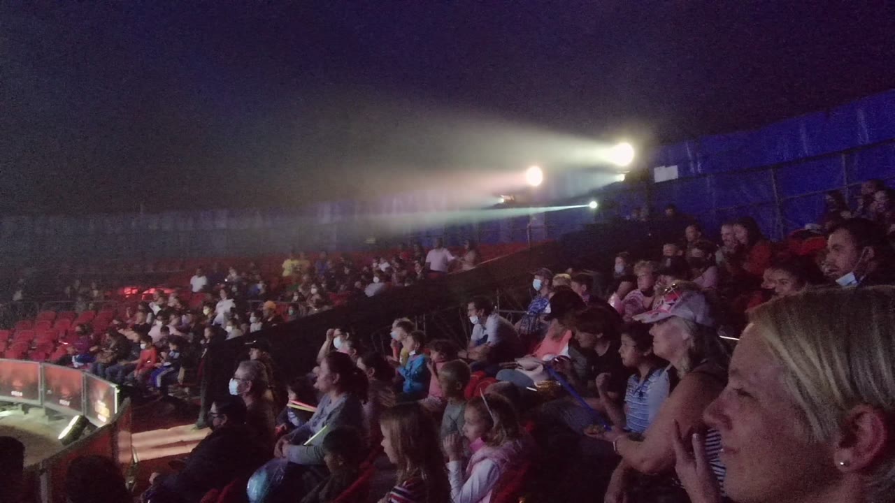 Crowd seated in a dark venue with a blonde woman in foreground.