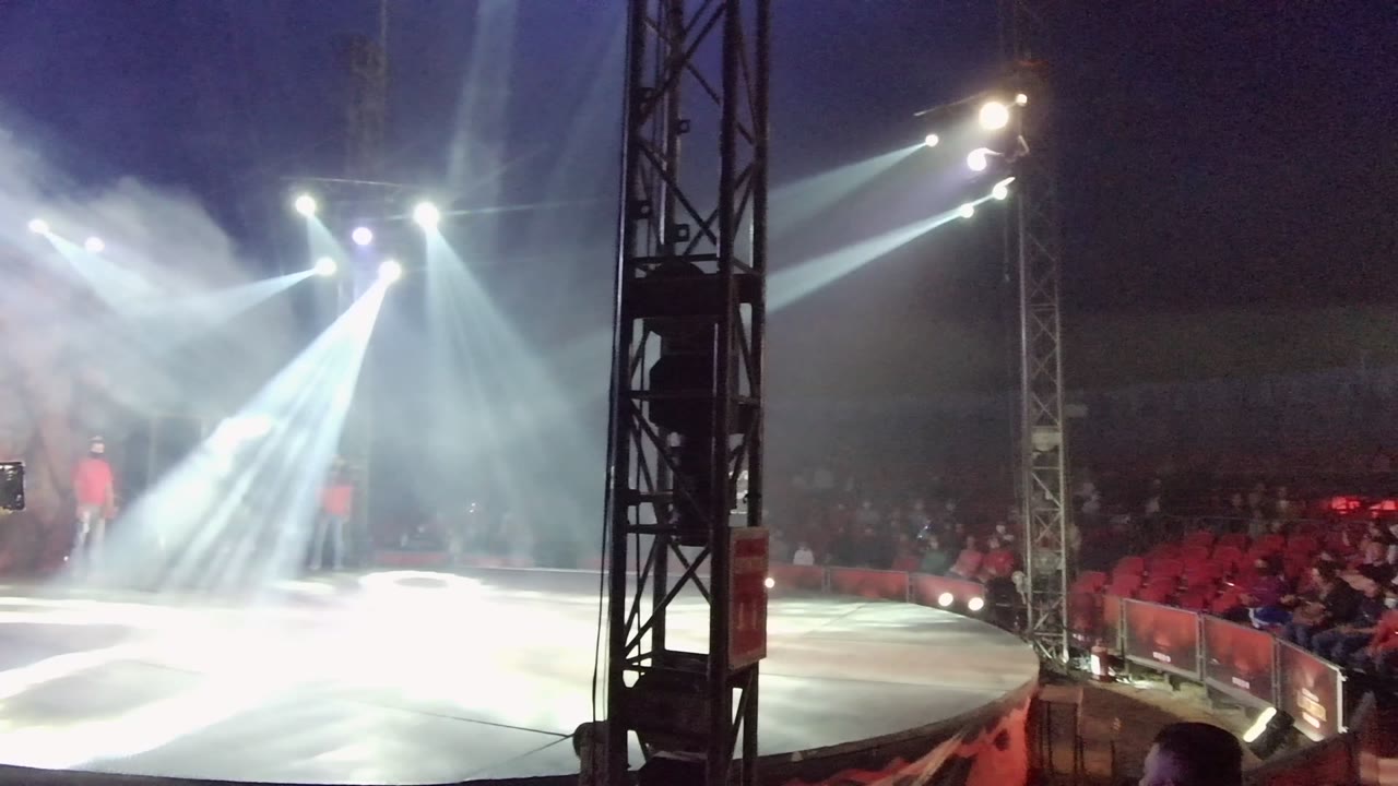 Spotlights and smoke cover the stage while a performer remains farther back.