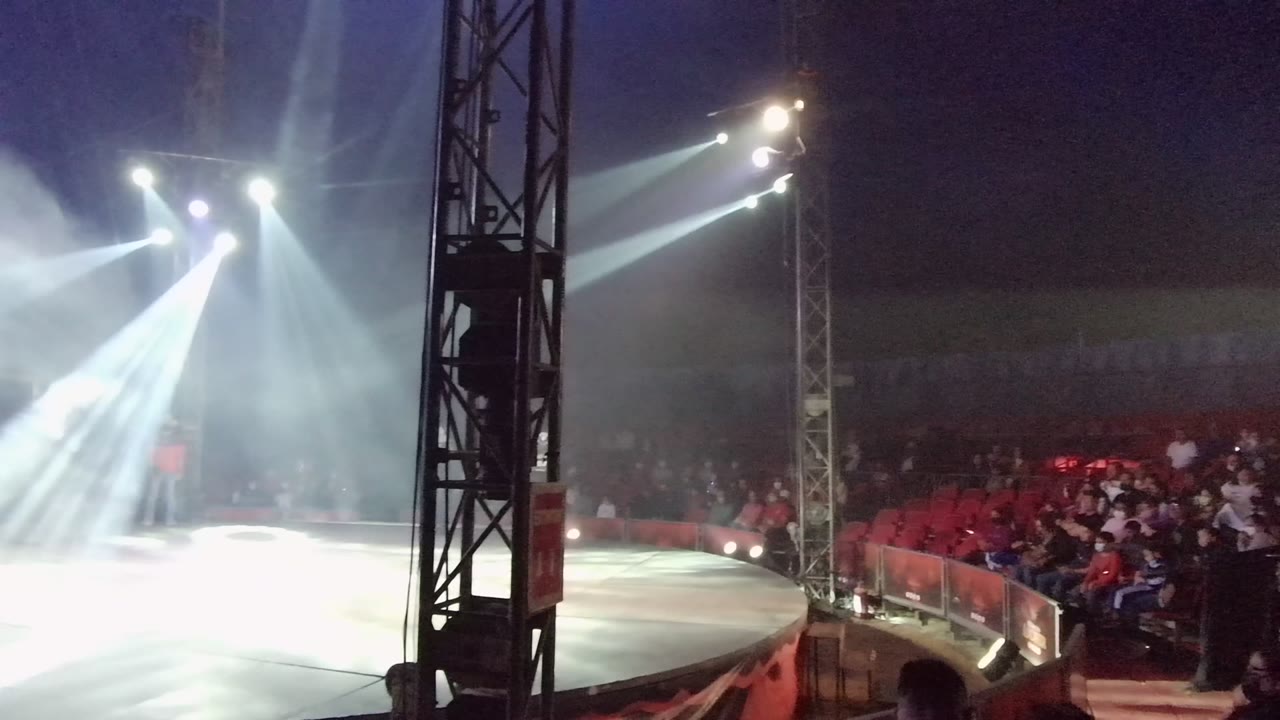 The stage side view in San Jose Del Cabo BCS Mexico shows a black truss in the foreground, heavy smoke in the light beams, and the red-seated audience filling the background.