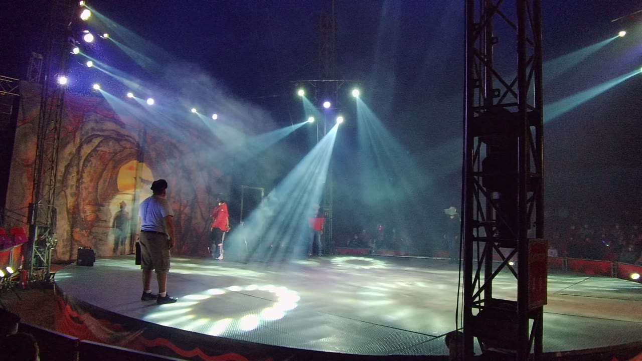 In San Jose del Cabo BCS Mexico, two red-shirted dancers move forward from the backdrop while smoke thickens around the white spotlights and the foreground person watches from the stage edge.