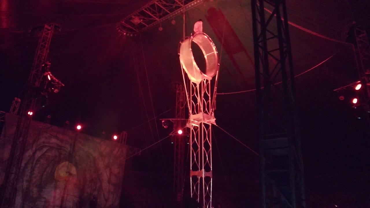 Glowing circular stage prop with an attached ladder hangs above a dark performance venue in San Jose del Cabo, Mexico, with red lights and no visible people.