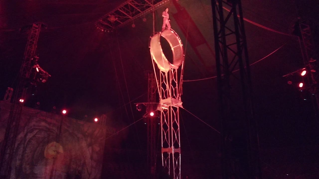 In San Jose Del Cabo BCS Mexico, a performer stands on top of a large aerial ring while red lighting and overhead stage truss frame the dark performance space.
