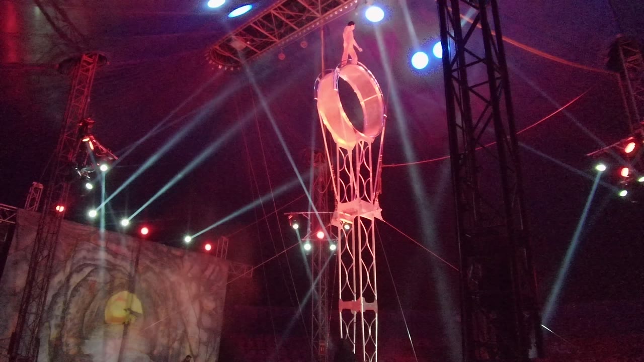 Suspended ring act with crossed light beams and stage rigging.