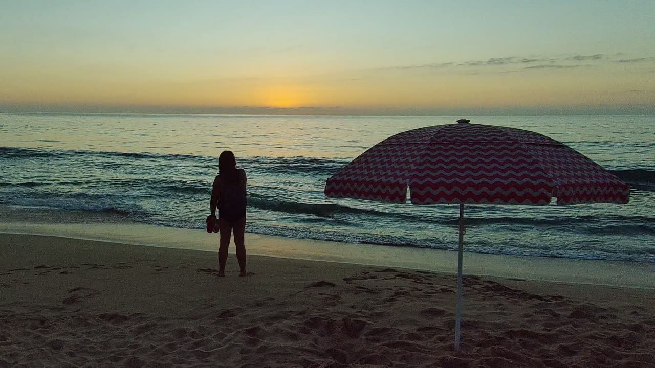 San Pancho Nayarit Mexico beach view with the foreground walker gone, a single silhouetted person near the water, and the striped umbrella occupying the right side of the frame.