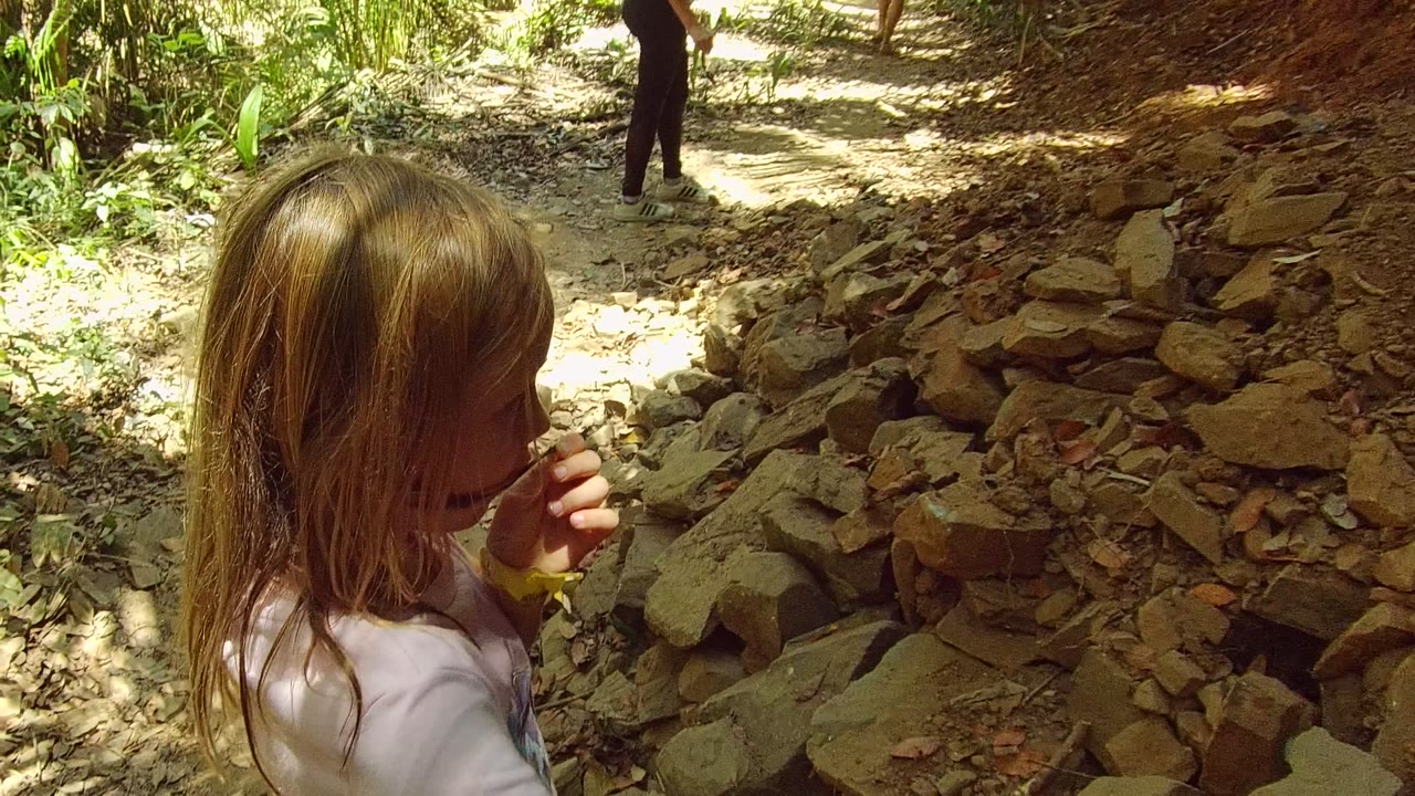 Girl in profile beside a rocky dirt bank on the forest path.