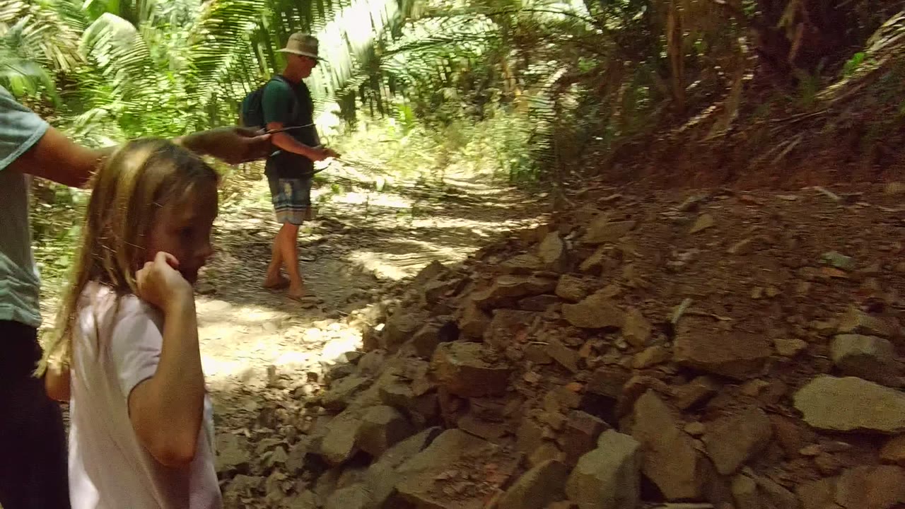 A child stands near the foreground while two adults walk ahead on a rocky forest trail in San Pancho Nayarit Mexico.