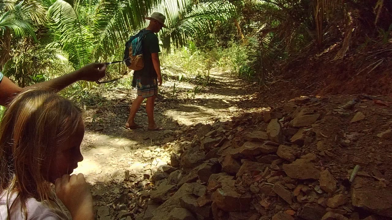A child is close to the camera in profile as an adult with a backpack walks farther up the rocky trail in San Pancho Nayarit Mexico.