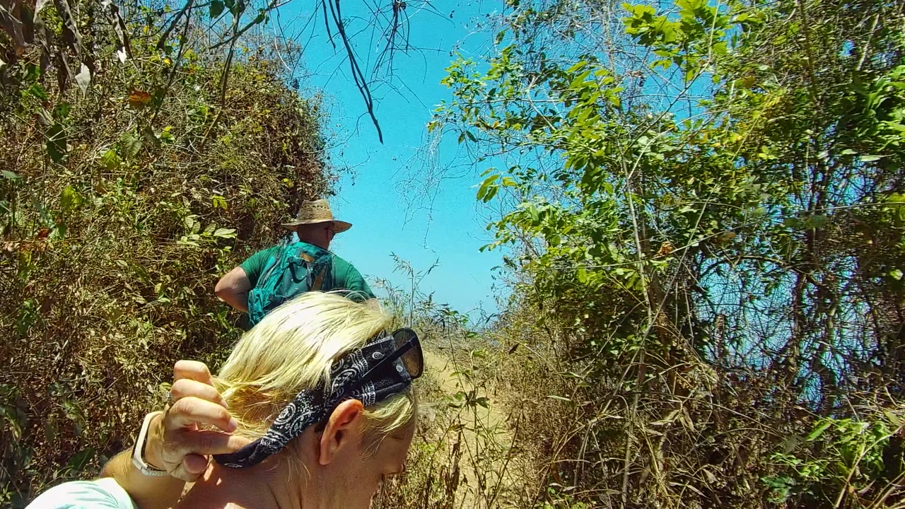The foreground person holds blond hair beside the camera while the hat-wearing hiker moves farther along the narrow San Pancho Nayarit Mexico path.