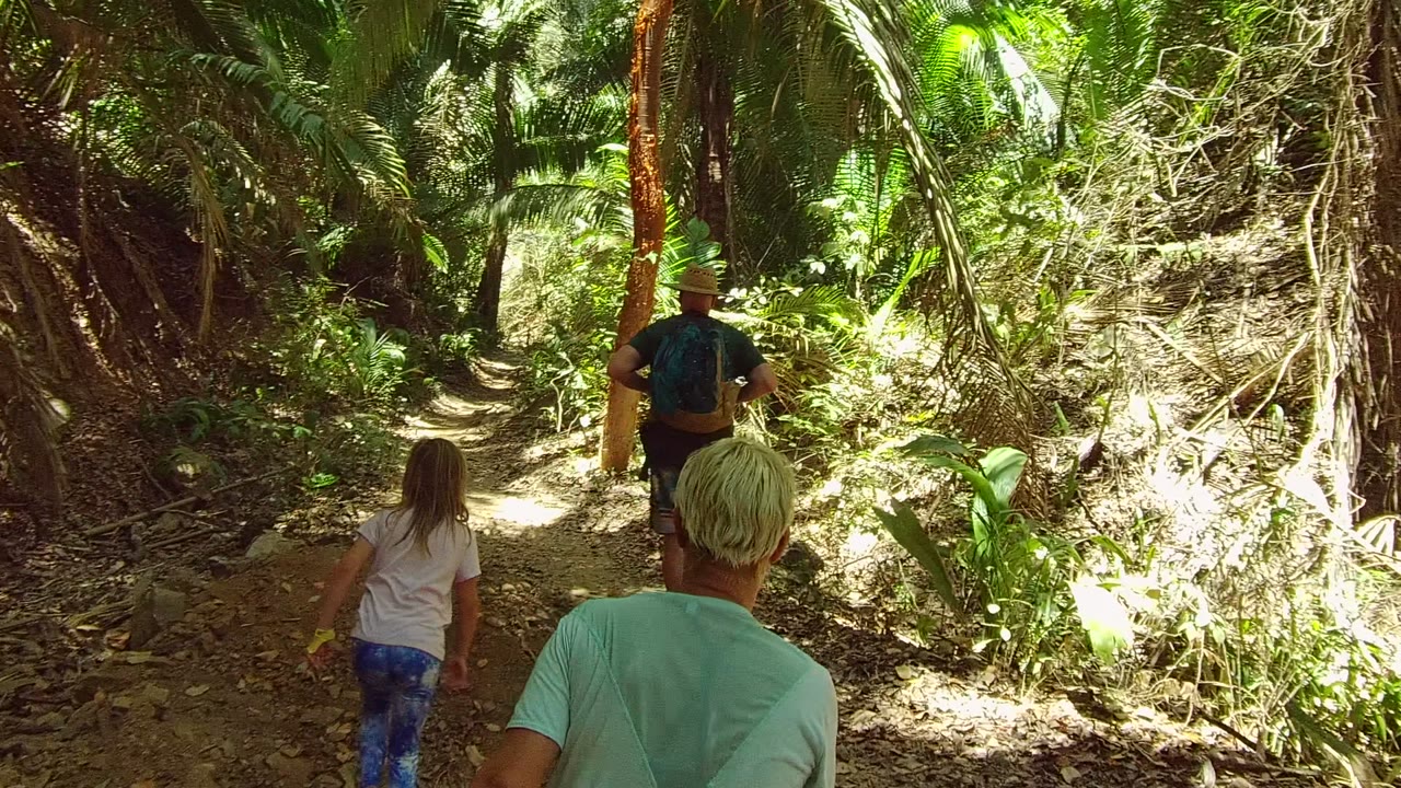 Child and adults continue along a narrow dirt trail.