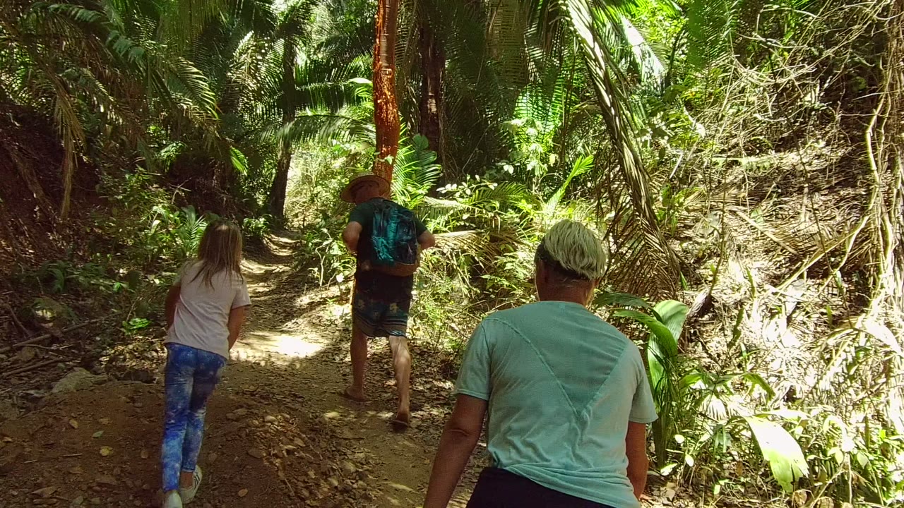 The group advances on the dirt path in San Pancho Nayarit, Mexico, with the lead hiker ahead, the child near center, and a light-shirted adult at the right edge.