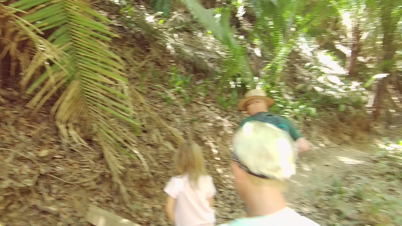 The group is farther ahead on the San Pancho Nayarit Mexico trail, with the blonde headscarf close to camera and a sunlit curve in the dirt path visible through dense greenery.