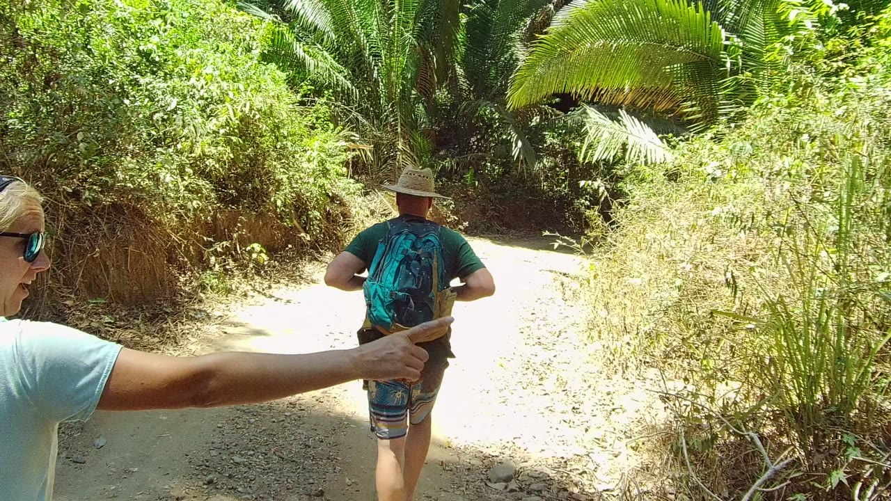 Light-haired hiker gestures while another hiker walks ahead on the trail.