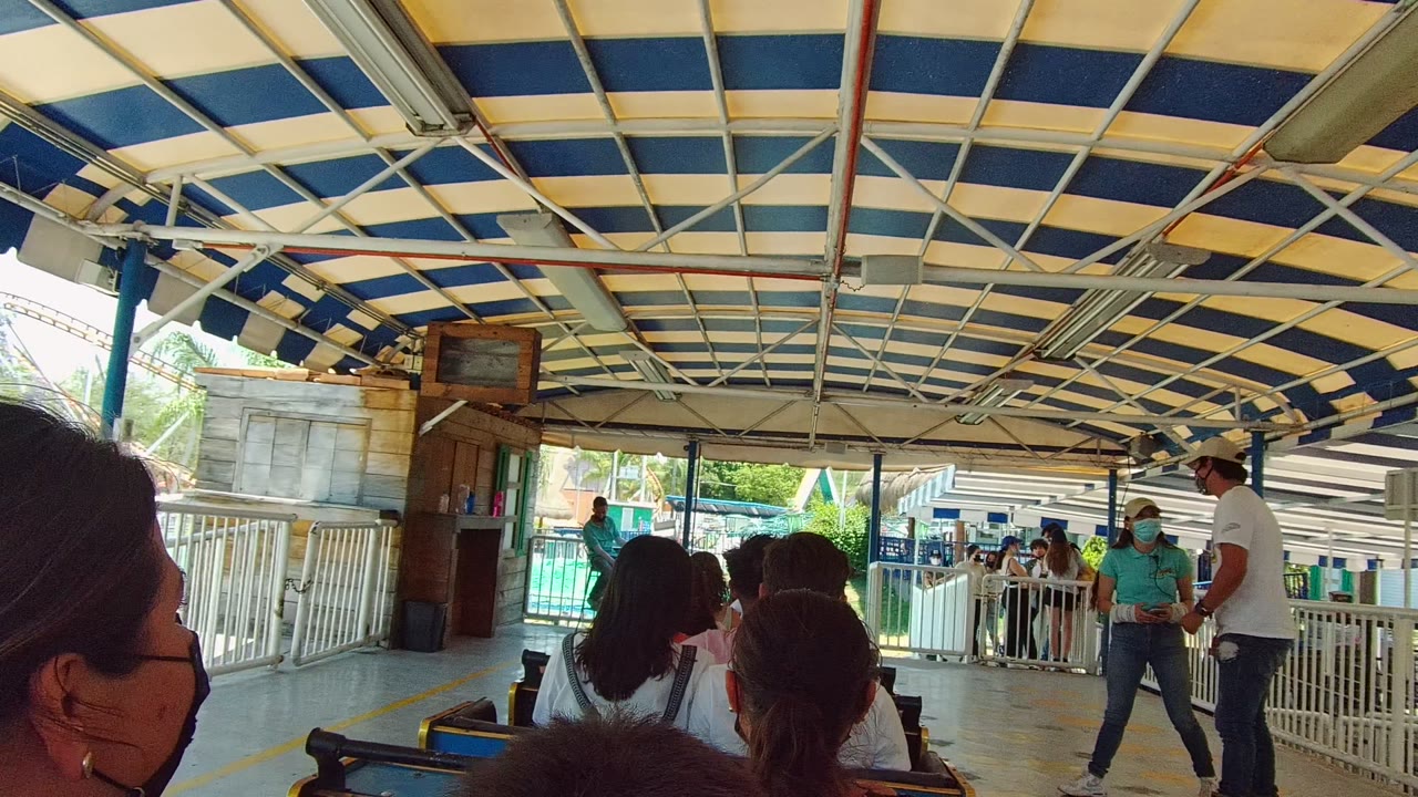 Passengers sit in the foreground while masked station staff stand near white railings under the blue and white canopy in Guadalajara, Mexico.