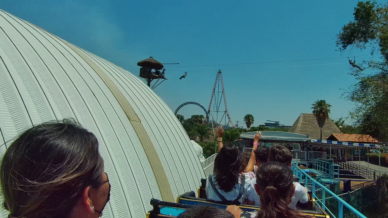 Ride passengers approach blue railings with roller coaster track in the background