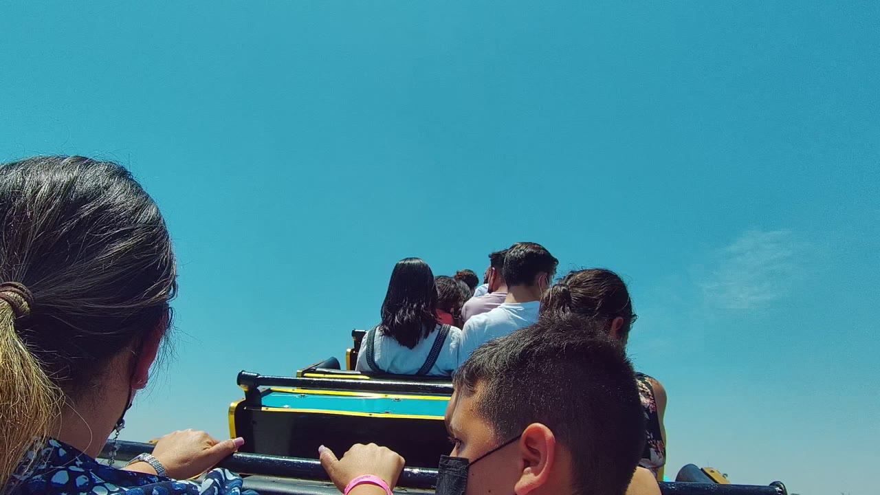 Woman and child in foreground behind riders on an open vehicle.