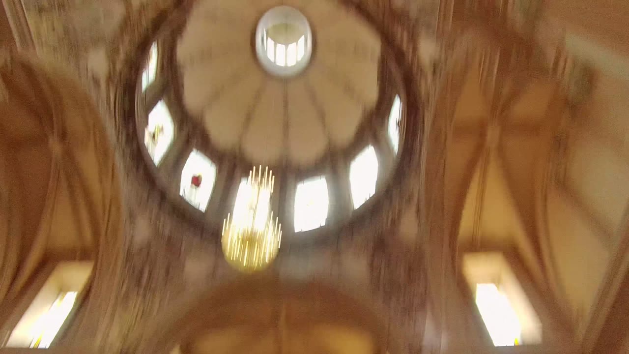 Upward view of a domed interior ceiling in Guadalajara, Mexico, with arched windows, a chandelier, warm light, and no visible people.
