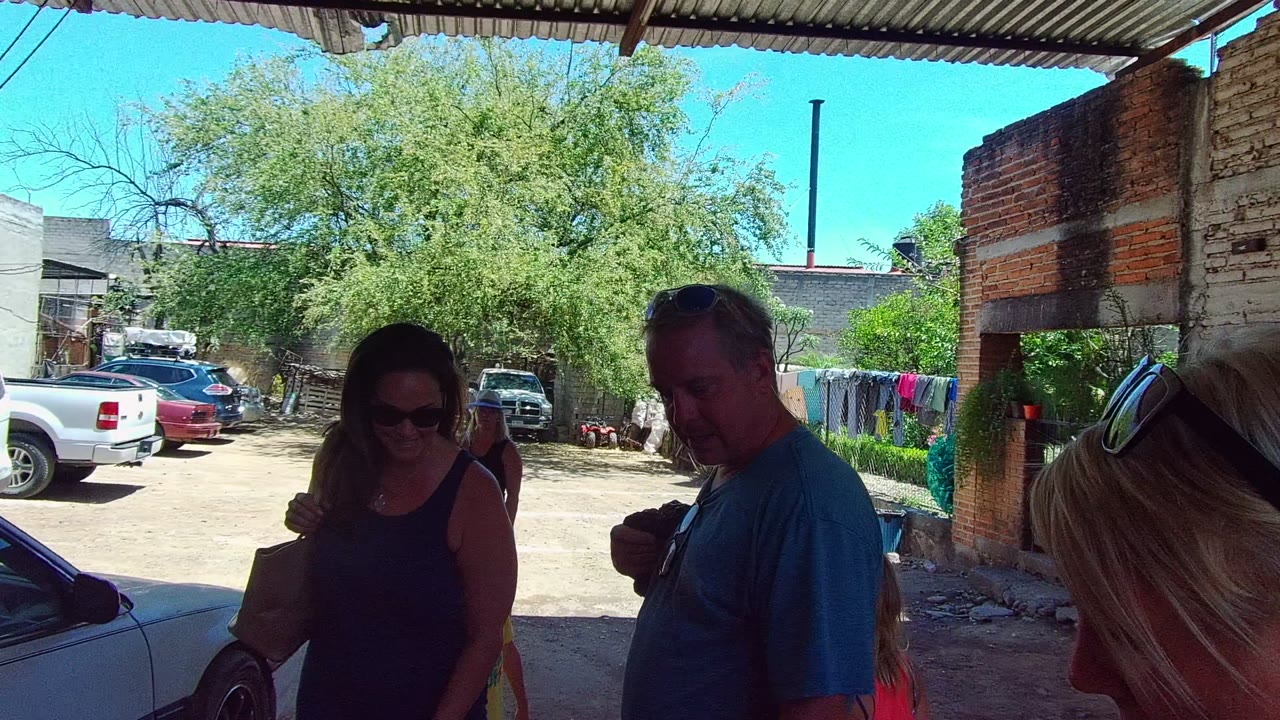 Woman with sunglasses and man in blue shirt standing in shaded courtyard.