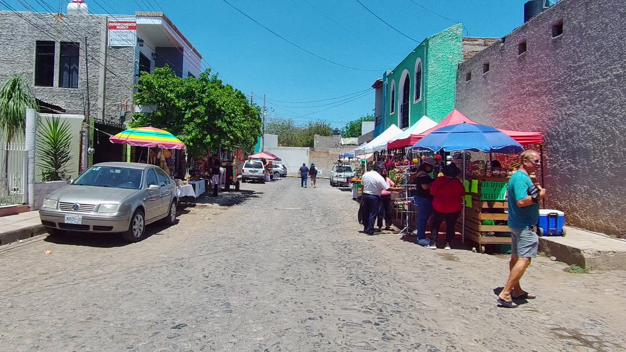 Woman walking past market stalls on a sunny cobblestone street