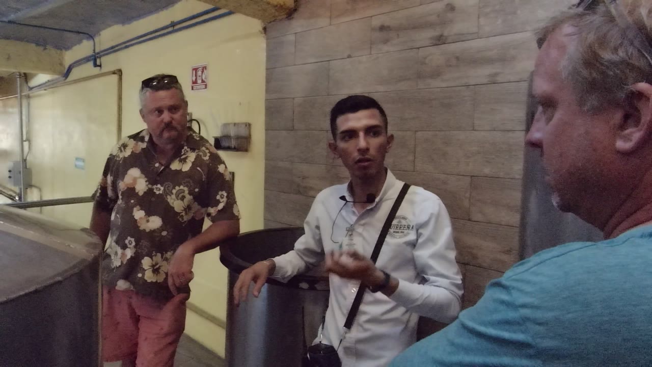The guide's hand lowers toward the tank area as the two adult visitors remain nearby in the industrial interior in Tequila Jalisco Mexico.