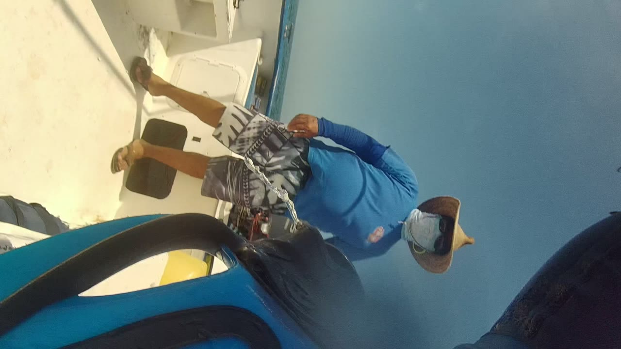 Person in blue shirt and hat standing on a boat under blue sky.