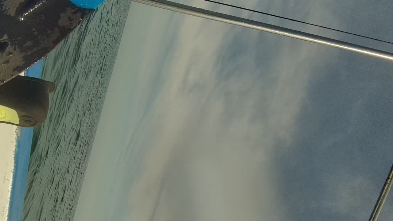 A tilted boat-side view in Cabo Pulmo, Mexico shows ocean water, cloudy sky, a white hull edge, and partial dark gear or clothing near the top of frame, with no visible people.