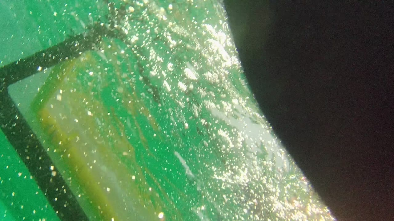 Close underwater frame in Cabo Pulmo, Mexico showing bubbles, a reflective gear surface, and dark diving equipment in green water, with no visible faces.
