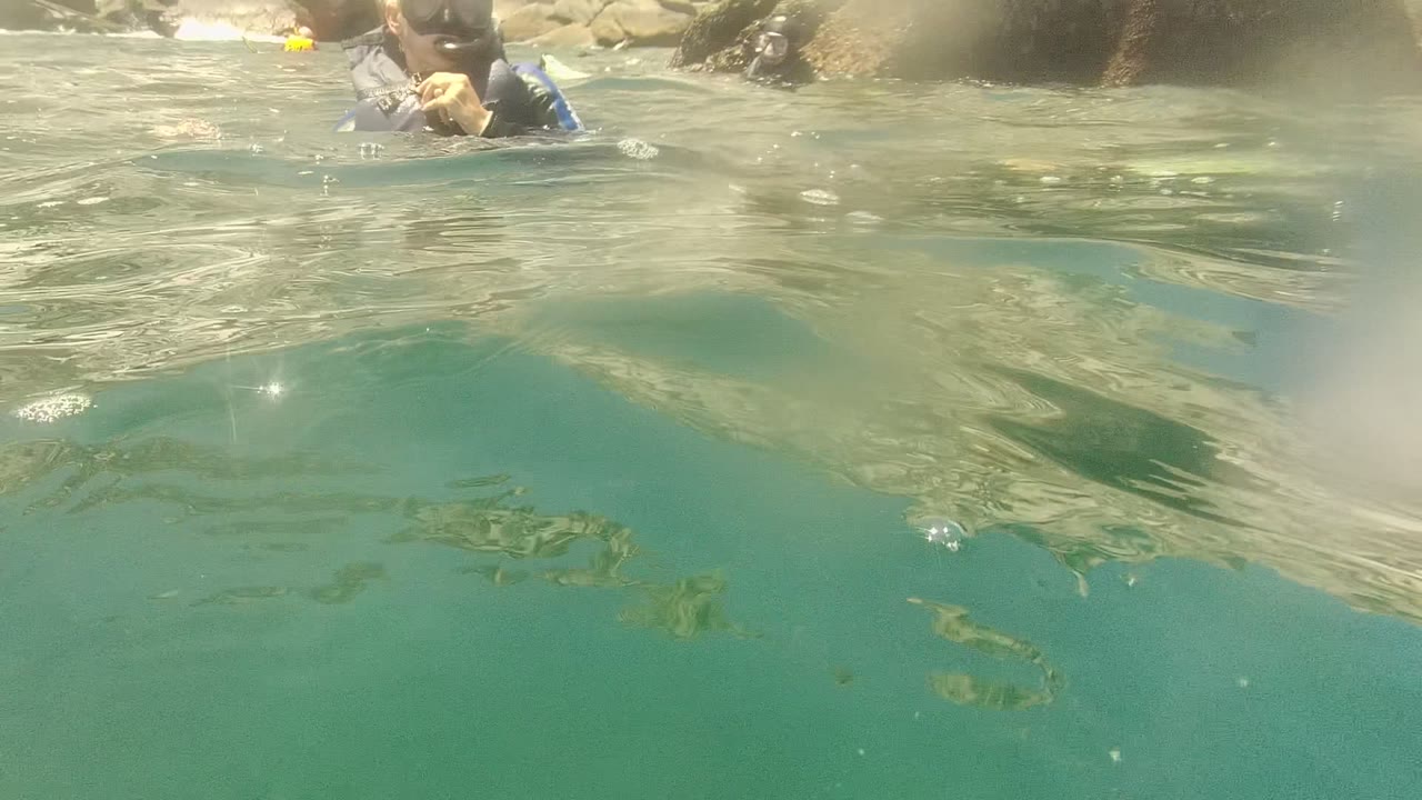 At Cabo Pulmo, Mexico, a partial snorkeler appears near the top edge while the camera looks through turquoise water toward rippled surface reflections.
