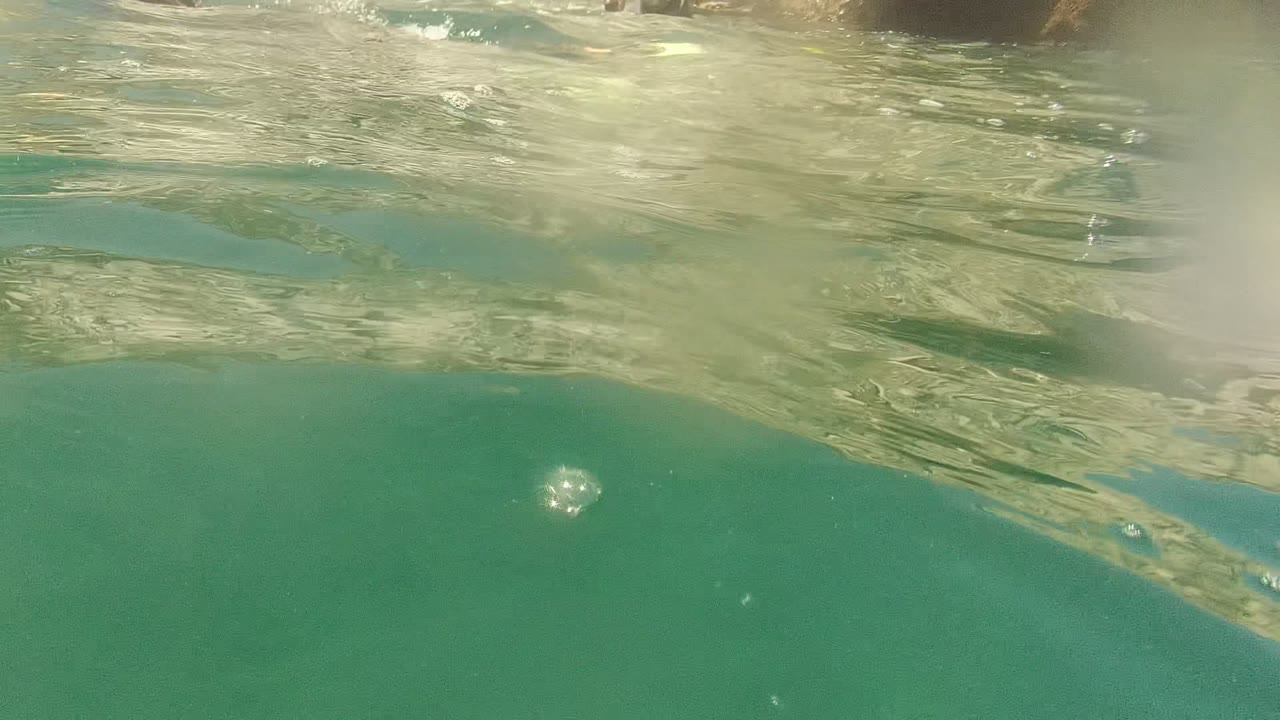 At Cabo Pulmo, Mexico, the frame shows clear green-blue water, a wavy reflective surface, a bright bubble in the upper midground, and no visible people.