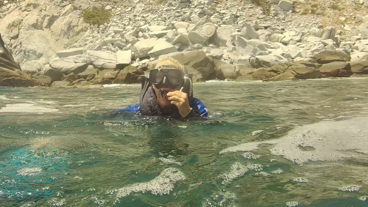 A snorkeler in a mask floats in green-blue water near the rocky shore in Cabo Pulmo, Mexico, with pale rocks behind them.