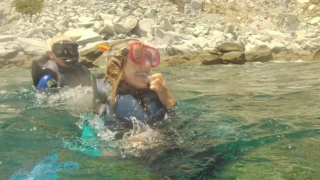 Two snorkelers in masks splashing in shallow coastal water.