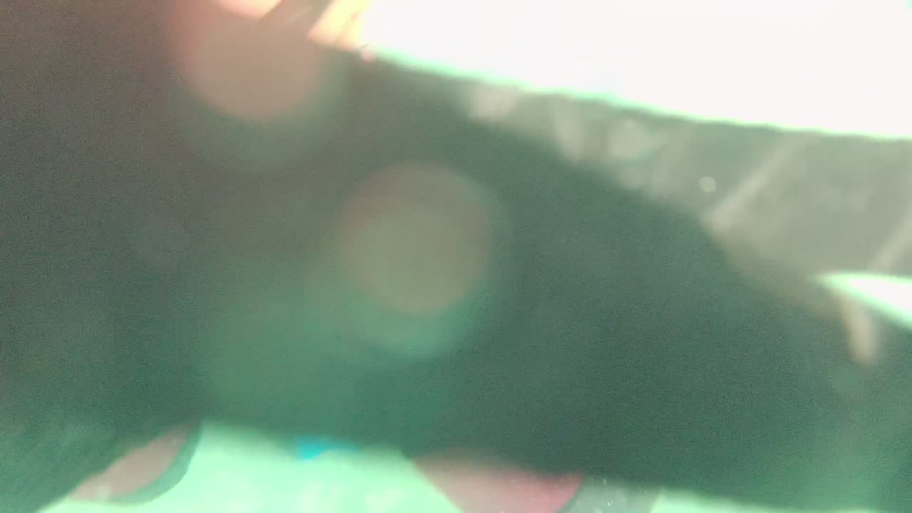 A dark wetsuit limb passes across the foreground in Cabo Pulmo, Mexico, with bright green underwater light and soft blurred particles around it.