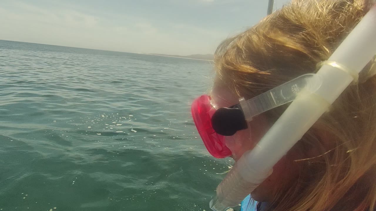 Close view in Cabo Pulmo BCS Mexico of a person wearing a pink snorkel mask near the edge of a boat, with green ocean water and a low hazy horizon behind.