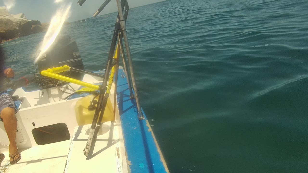 The boat edge and yellow equipment frame open green-blue ocean water in Cabo Pulmo, Mexico, with bright glare near the motor and no clear face visible.