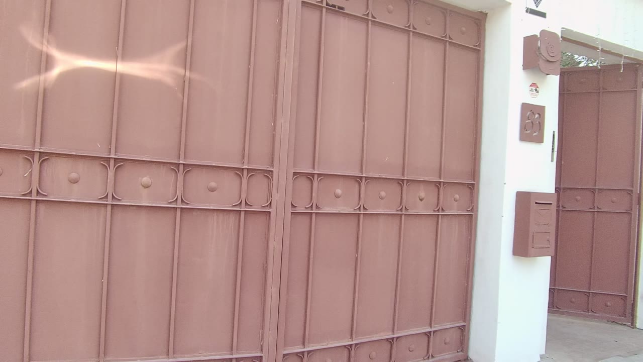 A person in a blue shirt, black shorts, and sneakers moves through the reddish brown metal gate at a residential entrance in East Cape Los Cabos, Mexico.