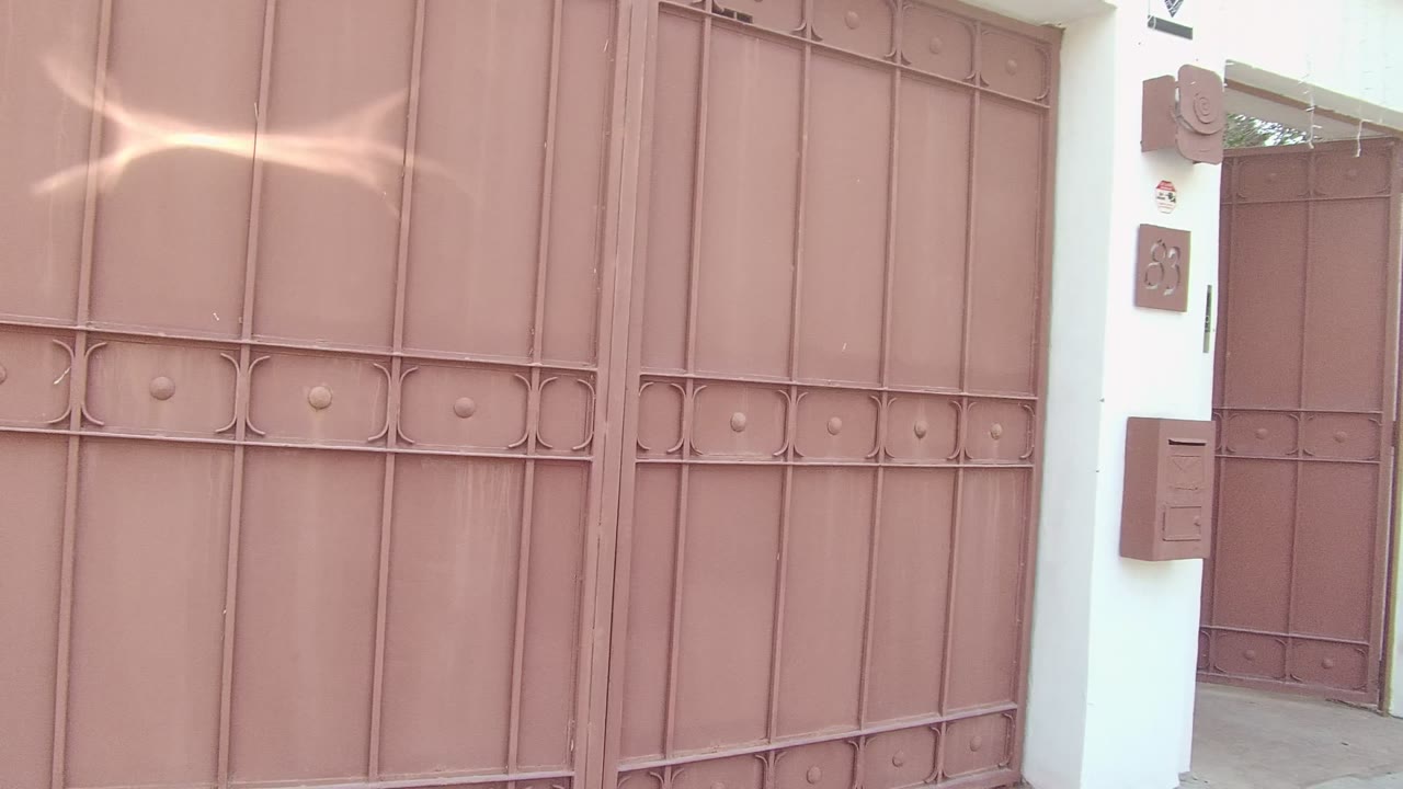 The reddish brown metal gate fills the frame again in East Cape Los Cabos, Mexico, with a bright reflected streak across the upper panels and no visible people.