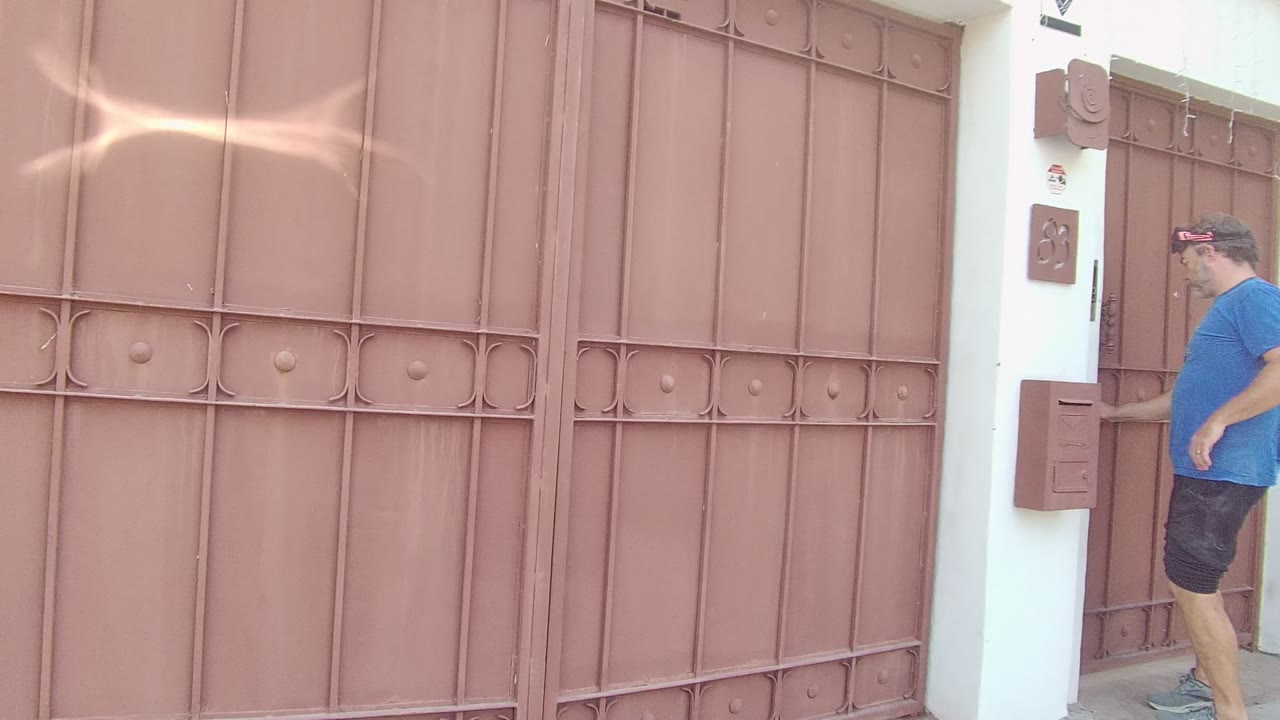 In East Cape Los Cabos, Mexico, the man in the blue shirt is near the wall-mounted intercom area at the right edge of the brown gate.