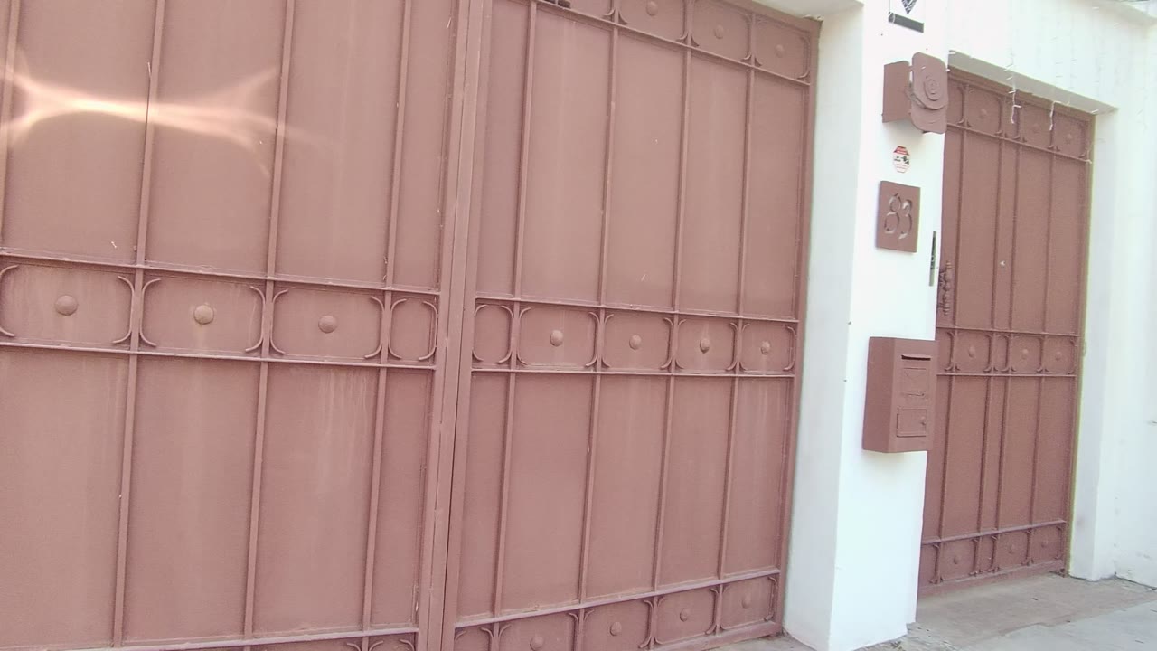 Brown metal gate with decorative bars and a white wall at the side.