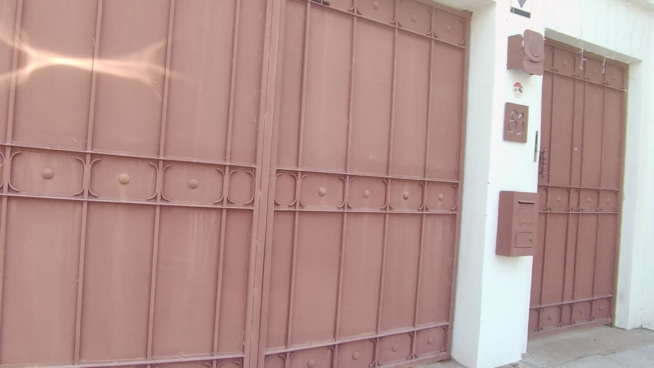 Closed brown metal gate in East Cape Los Cabos, Mexico, with mailbox and intercom details on the white wall to the right and no visible people.