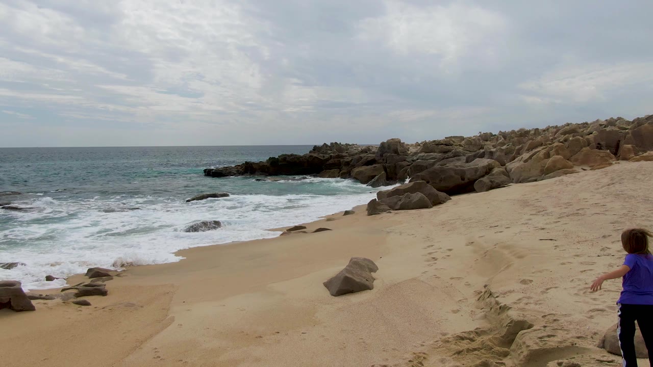 Child stands near the right edge as waves wash onto a sandy beach.