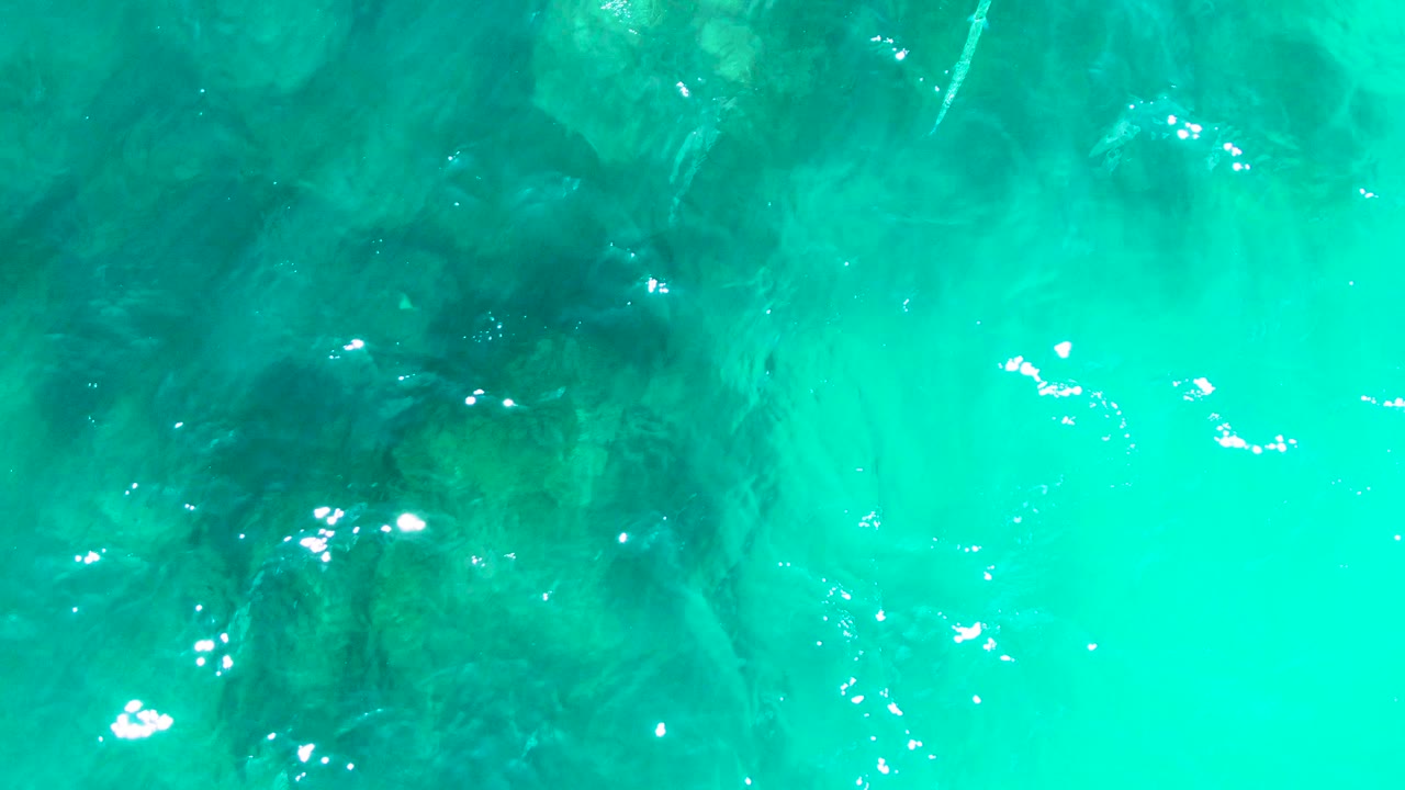 Turquoise ocean water at Buzzards Beach East Cape BCS Mexico reveals darker rock shapes under the surface, with small white light reflections and no visible people.