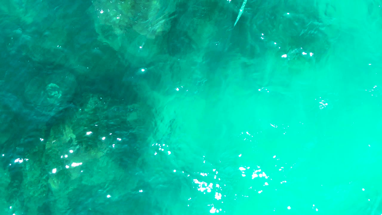 A bright patch of turquoise water at Buzzards Beach East Cape BCS Mexico crosses over submerged rock shadows, scattered sun sparkles, and no visible people.