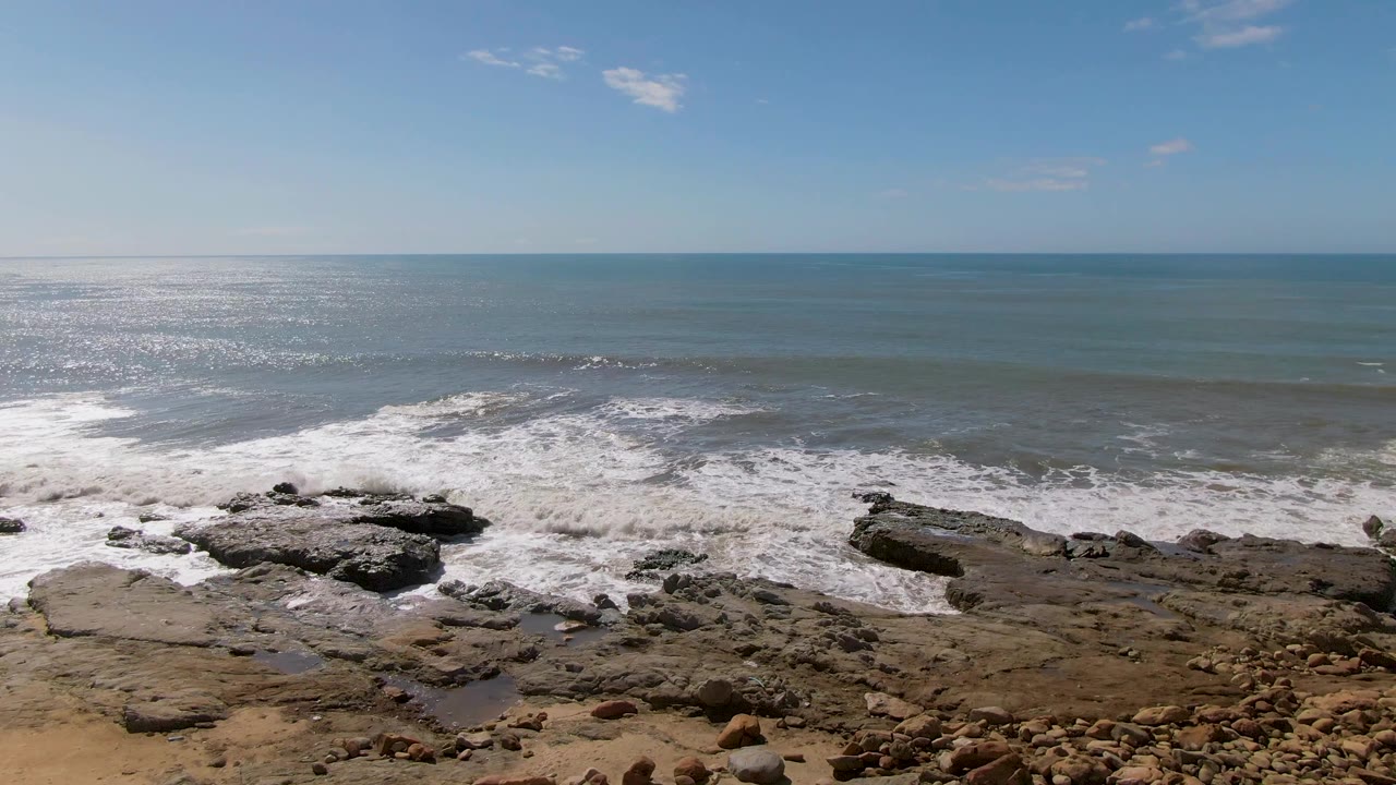 Rocky shoreline with white surf and sunlit ocean horizon.