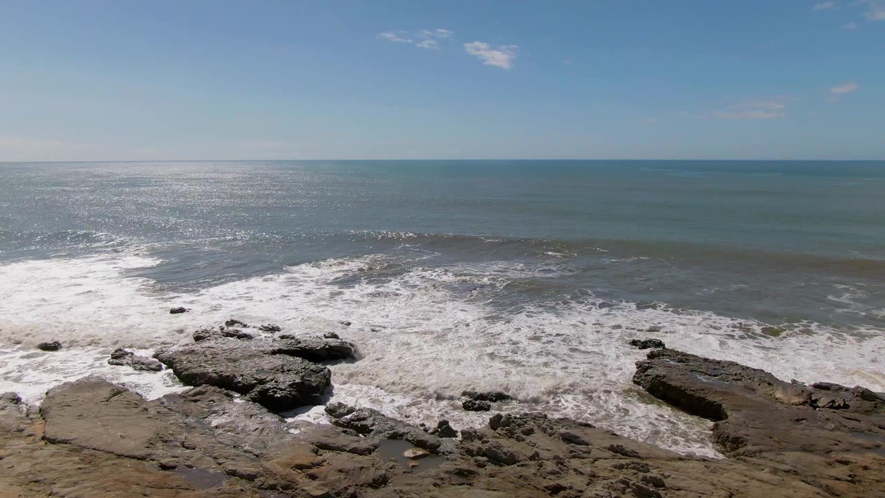 At Buzzards Beach in Mexico, a darker wave crest rolls toward the rocky shoreline as white foam spreads across the lower frame, with no visible people.